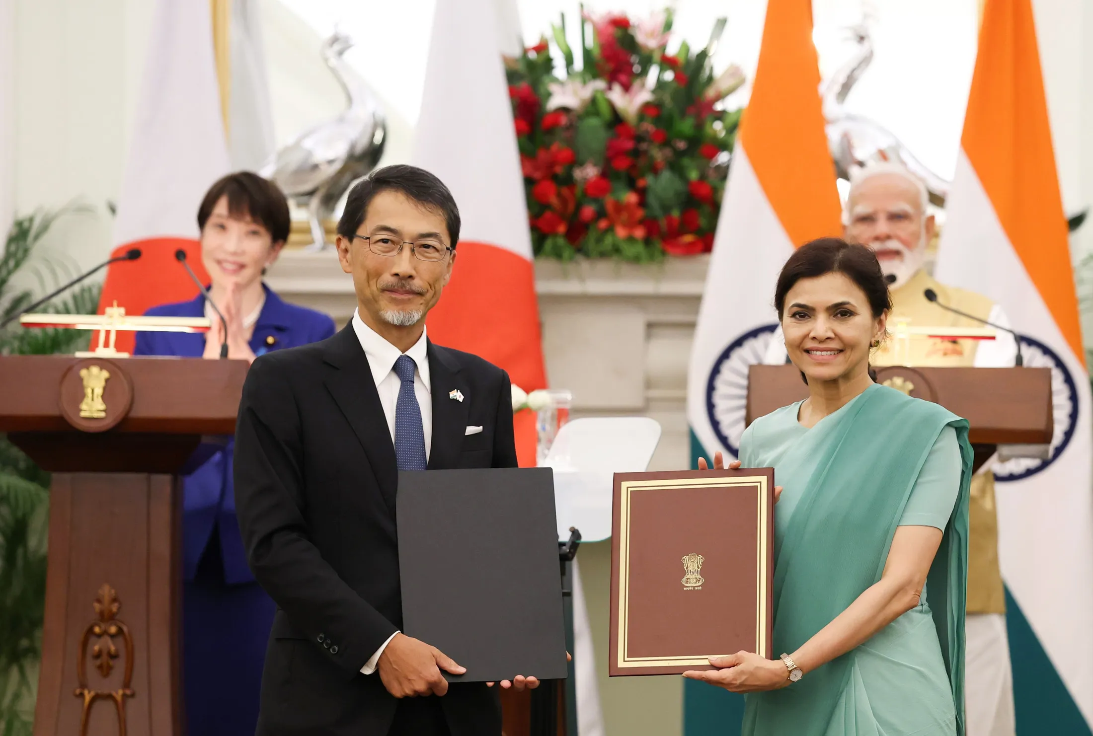 Indian and Japanese officials hold up signed agreements for the cameras at Hyderabad House, with Prime Ministers Modi and Takaichi watching from behind.